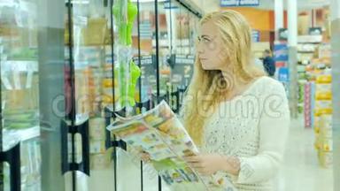 漂亮的女人在超市买食物。 带着广告优惠阅读报纸.. 把食物拿出来