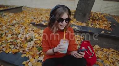 可爱的少女听耳机音乐，都市风格，时髦的时髦少女坐在城市街道的人行道上