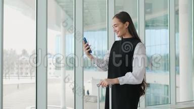女游客在国际机场航站楼携带行李使用智能手机。 语音识别短信命令