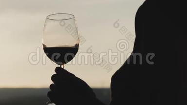 年轻女子喝着酒杯里的红酒，看着夕阳