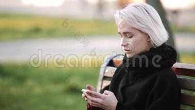 金发女孩在外面看着长凳上的智能手机在智能手机上玩一个活跃的3D游戏微笑