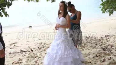 助理协助新娘在沙滩上系婚纱礼服