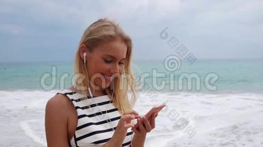 年轻漂亮的苗条女人，一头金发，穿着<strong>黑白</strong>连衣裙，站在海岸上，用智能<strong>手机</strong>