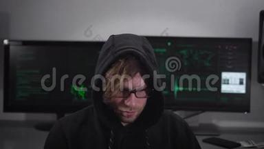 关闭一个间谍与智能手表坐和使用笔记本电脑与电脑显示器在他后面。 戴眼镜的罪犯