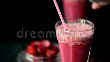 有一杯红冰沙，里面有牛奶，樱桃和草莓.. 在黑暗中，一块冰沙被倒入玻璃杯中