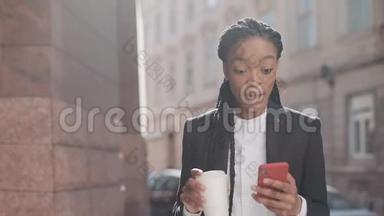 一位年轻的非洲裔美国女商人穿着西装，在城市里<strong>走来走去</strong>，喝着咖啡，用着