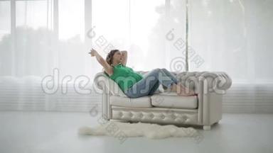 一个穿绿色衬衫的孕妇坐在沙发上抚摸着大肚子。