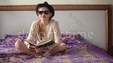 戴着太阳镜戴着帽子的小女孩看着照相机看书，微笑