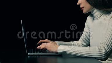 漂亮的黑发女人在黑色背景下的便携式电脑上打字。 4K视频