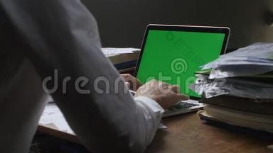 人工作在笔记本电脑晚办公室与绿色屏幕。 商人晚上和乔玛·凯一起在电脑里工作。