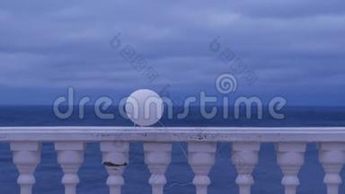 一个阴天，白色气球在风中系在海边的栅栏上。