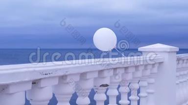 一个阴天，白色气球在风中系在海边的栅栏上。