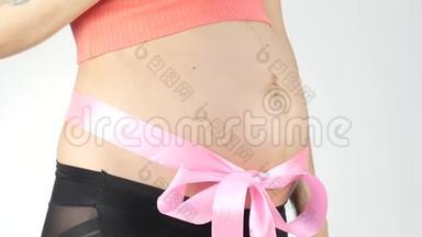 穿着内衣的怀<strong>孕妈妈</strong>在玩婴儿鞋。 腹部有粉红色的丝带。 4K