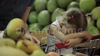 当妈妈在超市挑选水果时，宝宝很累地坐在购物车里