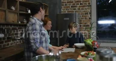 幸福的一家人在厨房做饭，而儿子则在拍摄父母和姐姐一起做饭的视频