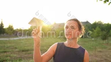 女人在日落的背景下发射纸飞机。 梦想旅行或空姐的职业