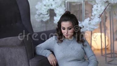 孕妇坐在扶手椅附近。 有灯光的<strong>床背景</strong>。 美丽的女人在家里度过时光
