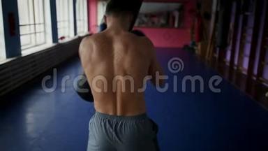 男拳击手的后视在健身房为拳击手套打拳。 职业拳击手进行拳击训练