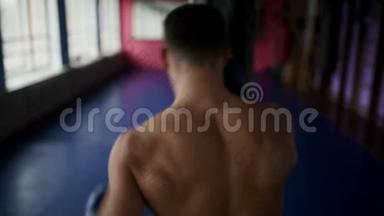 男拳击手的后视在健身房为拳击手套打拳。 职业拳击手进行拳击训练