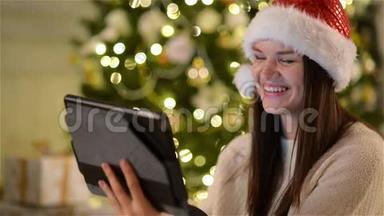 圣诞老人帽中美丽的女士在圣诞树上庆祝圣诞节时，用摄像机呼叫某人