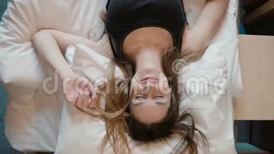 幸福的年轻女人倒在房间里的床上。 美丽的女孩微笑着，睁开眼睛，看着相机。
