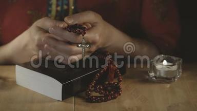 女人`手拿着一个十字架和念珠在一个封闭的圣经。