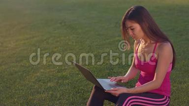 在绿草上<strong>用笔</strong>记本电脑工作的亚洲女人。 有魅力的女人<strong>用笔</strong>记本