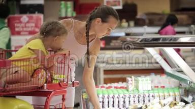 年轻的母亲带着女儿在手推车里挑选超市里的切水果