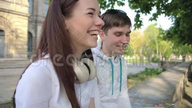 男生和女生，学生，坐在公园里，在电话里拍视频，然后大笑