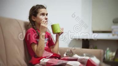 少女吃三明治喝茶看电视。 女孩吃三明治猫想在室内吃