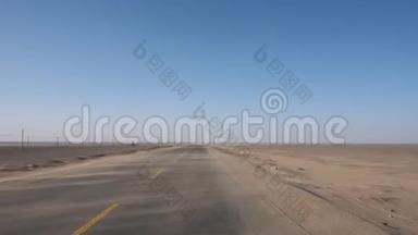 有人在空旷的沙漠道路上驾驶一辆汽车，沙子随风在道路上移动的观点。