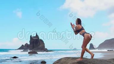 美丽的金发女孩穿着黑色上衣，在<strong>瑜伽</strong>中放松，在<strong>紫色</strong>的垫子上摆莲花，对抗海浪在岩石上奔跑