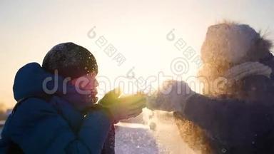 女孩和男孩在日落的背景下用手吹雪。冬季雪景。日落时间