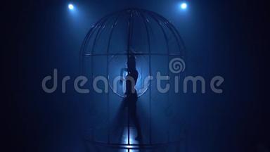 笼子里的女孩在黑暗的房间里用抱箍特技表演。 蓝色烟雾背景。 <strong>剪影</strong>。 慢<strong>动作</strong>