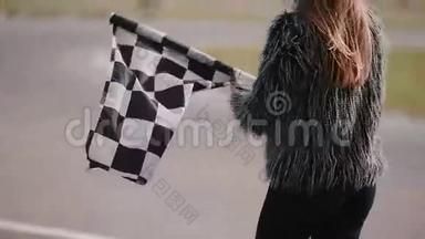一个女人的后景是举着一面挥舞的种族检查旗。 卡丁车赛道。