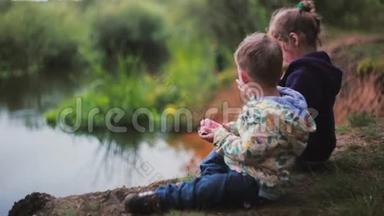 侧面看到两个可爱的小孩子，一个男孩和一个女孩，吃西瓜，坐在河岸上。