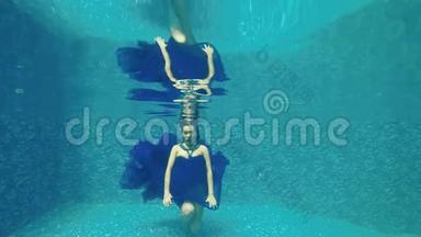 穿着蓝色长裙的漂亮女孩在泳池水下摆姿势拍照