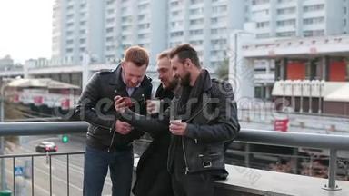 三个英俊的年轻人留着胡子，用智能手机。 三个英俊的年轻人靠近一座桥栏杆。 慢节奏