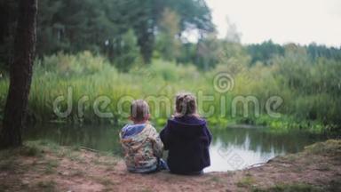 两个小孩，一个女孩和一个男孩坐在河岸上。 一个女孩在吃西瓜，他们回头看。 回顾
