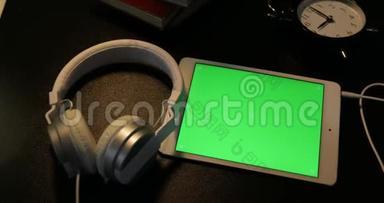 数码平板电脑上的绿色屏幕和晚上书桌上的耳机的多利拍摄