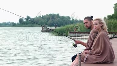 寒冷的早晨在湖边，年轻的情侣在河边钓鱼，相爱的情侣，坐在码头上的情侣
