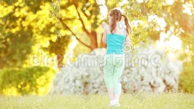 阳光明媚的夏日，可爱的小女孩在公园的树下散步。