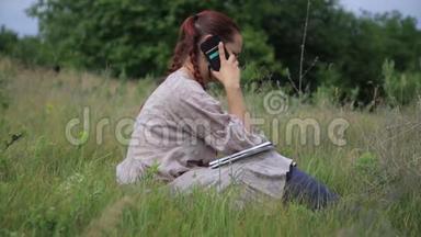 年轻漂亮的女人坐在夏<strong>季</strong>城市公园的草地上，用<strong>手机</strong>聊天。