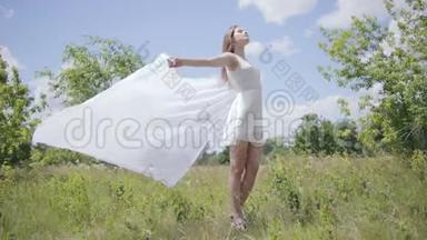 年轻漂亮的女人在风中拿着白色的布。 全程拍摄。 慢动作
