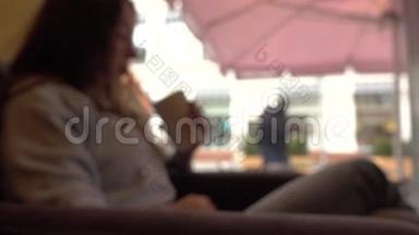 一个头发模糊的黑发女孩在<strong>窗边</strong>的一家咖啡馆里拿着吸管喝酒。 4K<strong>背景</strong>boke剪辑