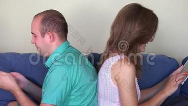 夫妻俩用自己的平板电脑背靠背坐在沙发上
