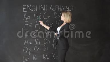 老师正<strong>在</strong>用粉笔<strong>在黑板上写字</strong>母表。 小学教育理念。
