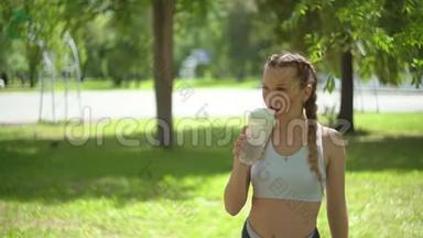 苗条的年轻女人在训练后<strong>喝水</strong>。 女运动员<strong>休息</strong>，她<strong>喝水</strong>，在炎热的跑步中外出