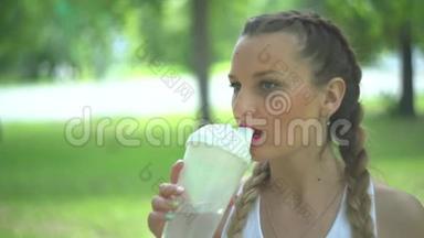 苗条的年轻女人在训练后喝水。 女运动员休息，她喝水，在炎热的跑步中外出