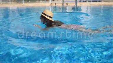 年轻漂亮的女孩戴着太阳镜和帽子在游泳池游泳。 在阳光明媚的日子里，女人在清澈的温水中放松。 夏季